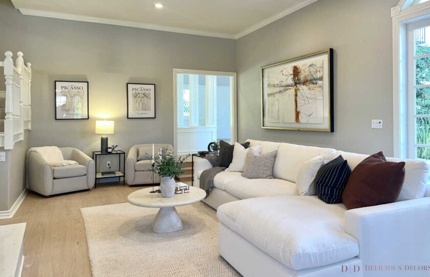Family room staged with large white sectional, round stone coffee table, grey armchairs, and framed Picasso exhibition prints.
