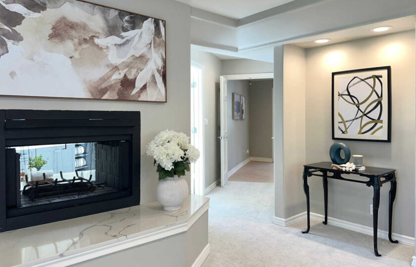 En-suite hallway staged with black accent console table, modern ring art, white hydrangeas, and double-sided fireplace.