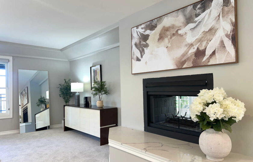 Primary bedroom sitting nook staged with dual-sided fireplace, marble hearth, white credenza, and full-length mirror.