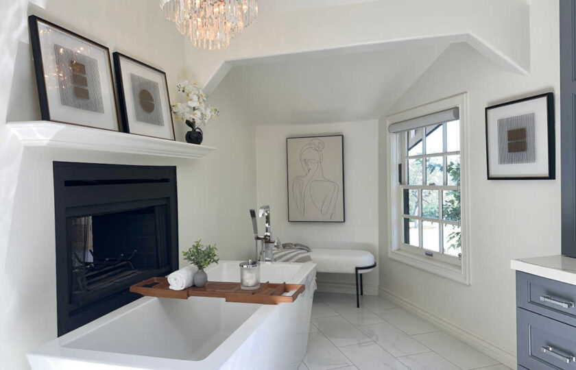 Primary bathroom staging showcasing freestanding tub, fireplace, crystal chandelier, and abstract line art.