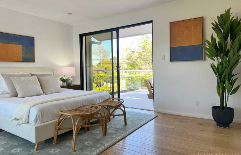 Light-filled Malibu bedroom staging highlighting neutral linens, rattan benches, modern abstract art, and potted indoor foliage.