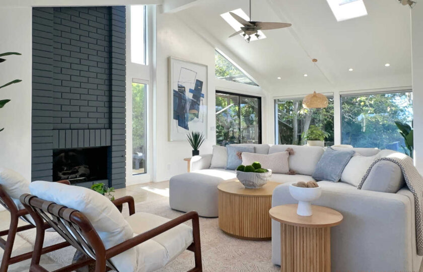 Mid-Century Modern staging in Malibu living room featuring fluted wood coffee table, curved light sectional, and dark brick fireplace.