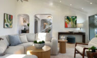 Staged Malibu great room showing arched entryways, dark wood console table, leaf art prints, and mid-century leather accent chairs.