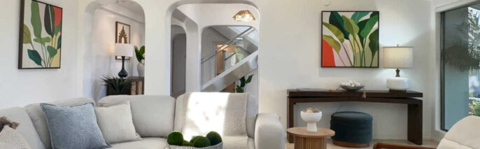 Staged Malibu great room showing arched entryways, dark wood console table, leaf art prints, and mid-century leather accent chairs.