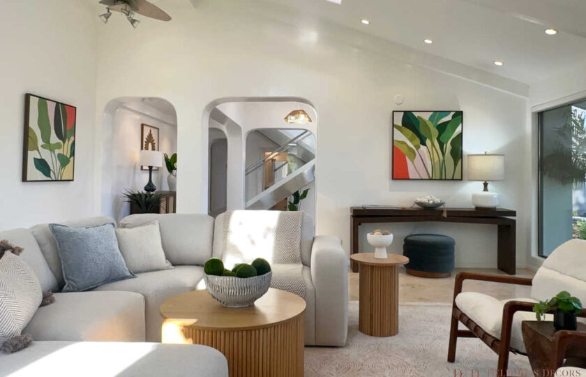 Staged Malibu great room showing arched entryways, dark wood console table, leaf art prints, and mid-century leather accent chairs.