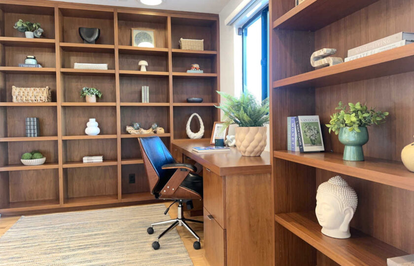 Mid-Century Modern home office staging in Malibu featuring floor-to-ceiling wooden bookshelves, warm wood desk, and executive chair.