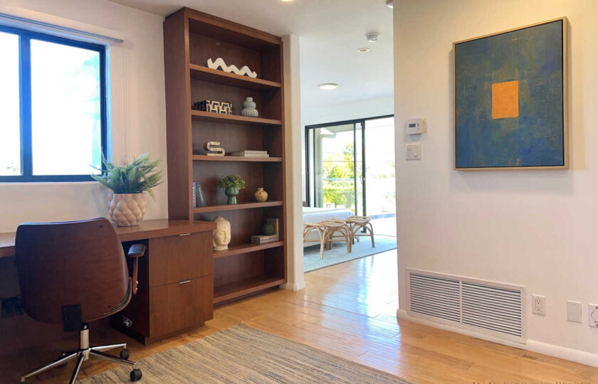 Staged Malibu study featuring custom dark wood built-ins, executive desk, geometric blue wall art, and hallway view.