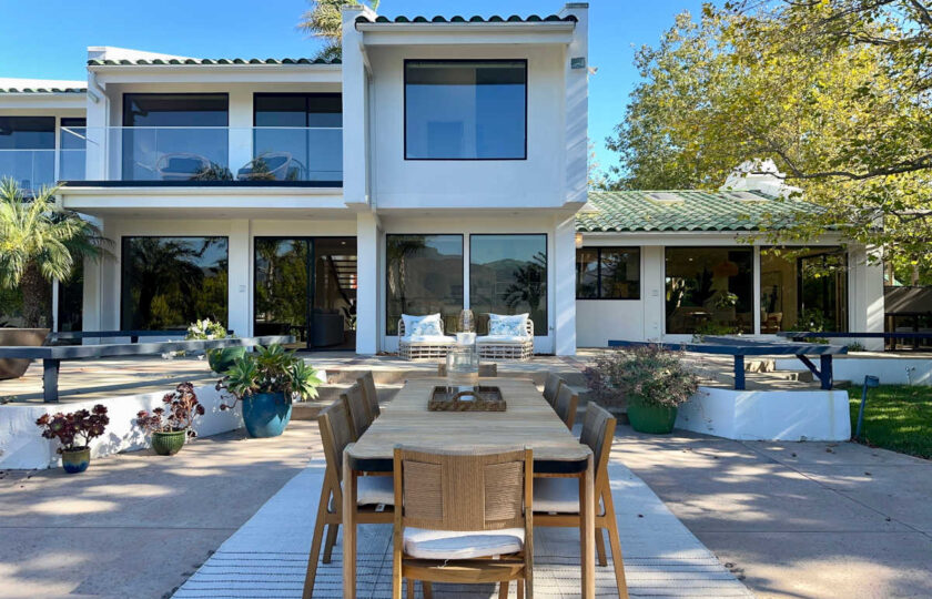 Modern Malibu home exterior featuring outdoor dining table, neutral area rug, and custom architectural patio staging.