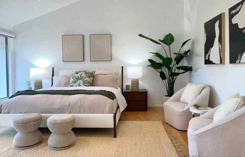 Primary bedroom staging featuring mid-century platform bed, cream bouclé armchairs, textured jute rug, and botanical artwork.