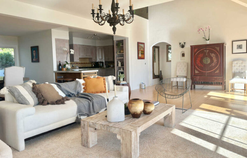 Open-concept Spanish Colonial home staging featuring a rustic coffee table, dark wood armoire, arched doorway, and wrought-iron details.