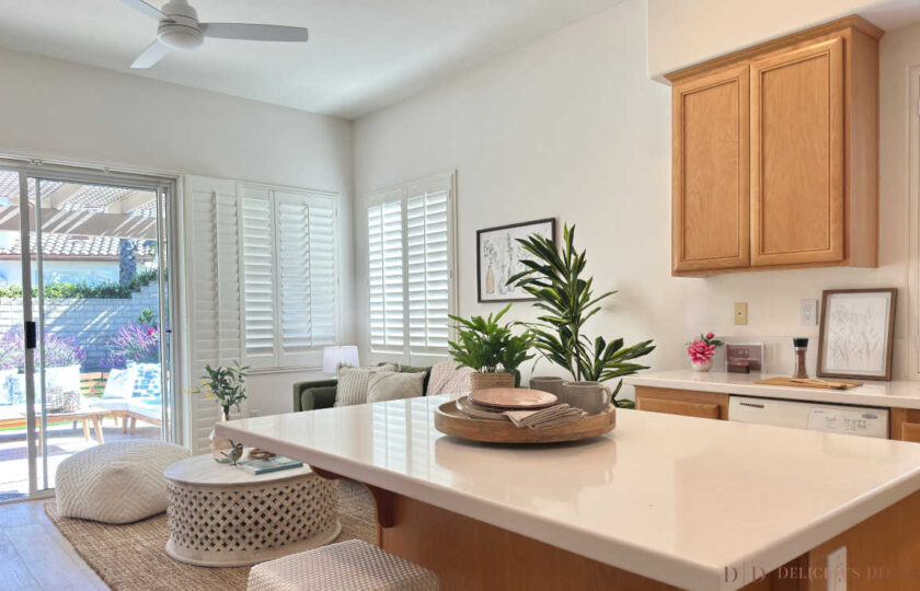 Kitchen island staging overlooking an open-concept family room with a green velvet couch and patio slider doors in Dos Vientos.