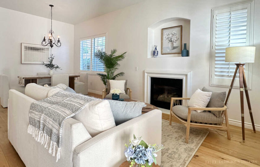 Coastal casual living room staging in Thousand Oaks showcasing a modern wood tripod floor lamp, light wood floors, and white plantation shutters.