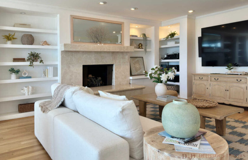 Malibu Cove Colony home staging showcasing custom white built-in bookcases, a stone fireplace, media console, and light oak hardwood floors.