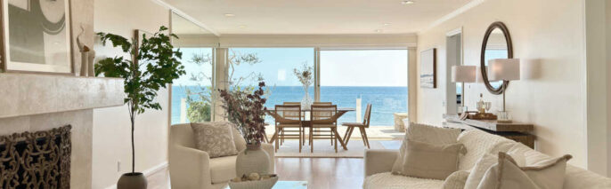 Malibu Cove Colony Home Staging featuring a luxury beachfront great room with white sofas, a stone fireplace, high-pile shag rug, and sweeping Pacific Ocean views.