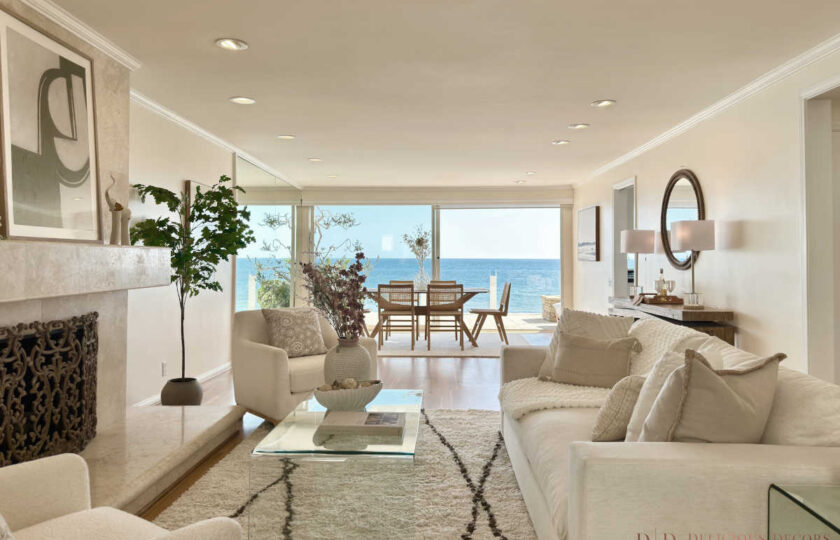 Malibu Cove Colony Home Staging featuring a luxury beachfront great room with white sofas, a stone fireplace, high-pile shag rug, and sweeping Pacific Ocean views.