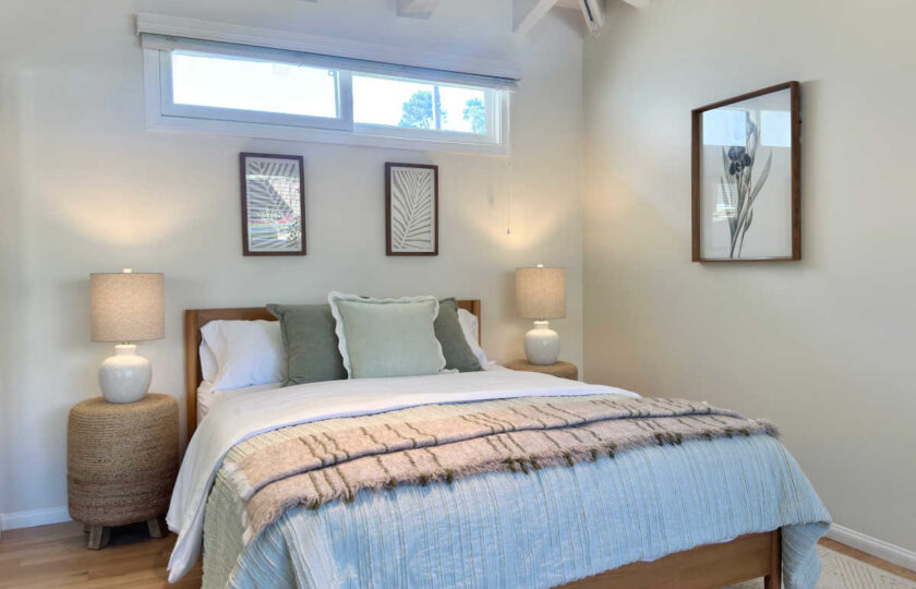 Coastal guest bedroom featuring a natural wood platform bed frame, sage green accent pillows, textured jute nightstands, and botanical wall art.