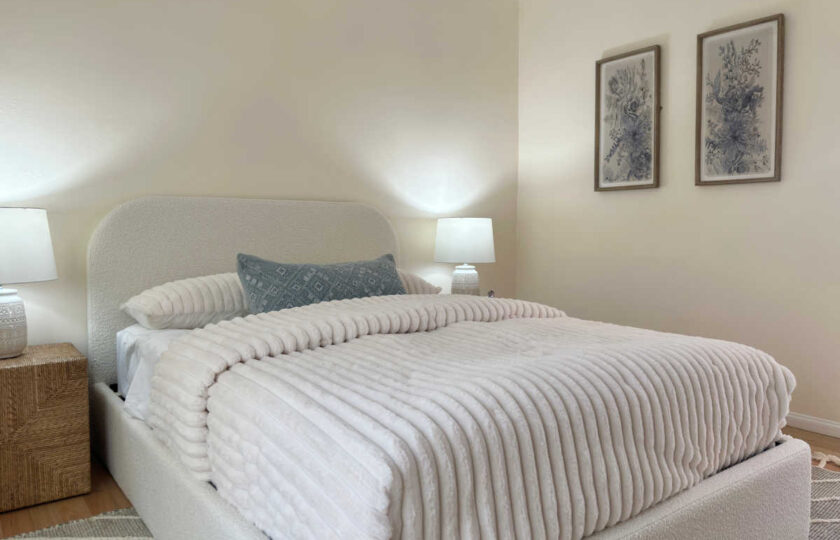 Alternate angle of a cozy guest bedroom featuring a low-profile cream bed frame, slate blue accent pillow, and framed floral prints.