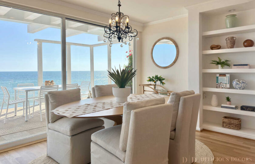 Casual coastal dining nook with linen upholstered chairs, a wrought iron chandelier, built-in shelving, and direct oceanfront balcony access.