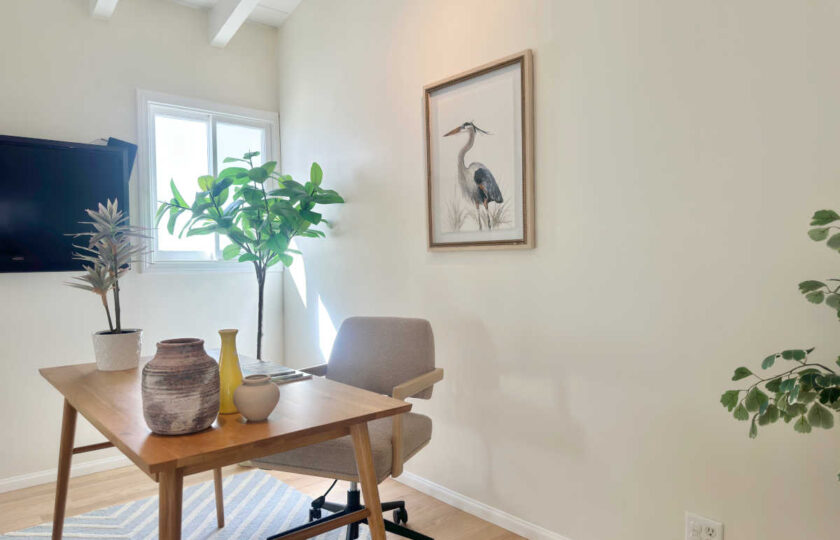 Minimalist home office staged with a mid-century wooden desk, woven wishbone chair, blue striped rug, and heron wall art in Malibu.