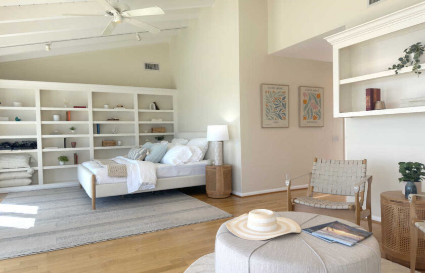 Sprawling primary bedroom suite featuring vaulted wood-beam ceilings, white built-in shelving, a neutral king bed, and an adjacent sitting lounge.