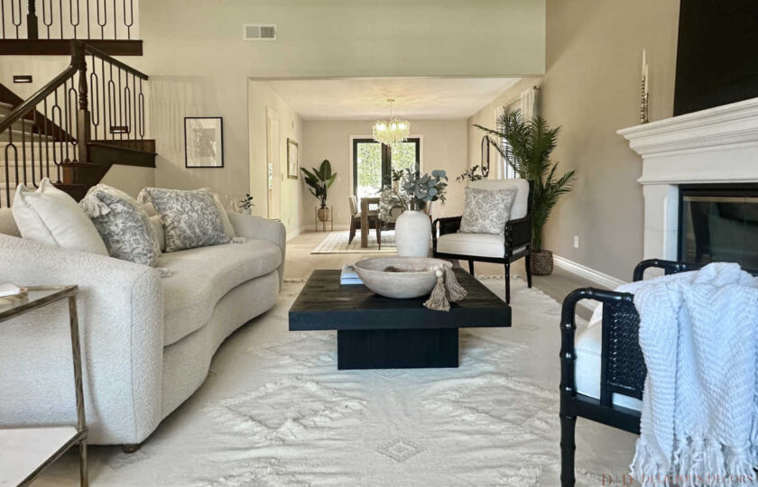Bright open-concept living area with Westlake Village home staging featuring a black wood coffee table, plush white rug, and dark wood staircase railing.