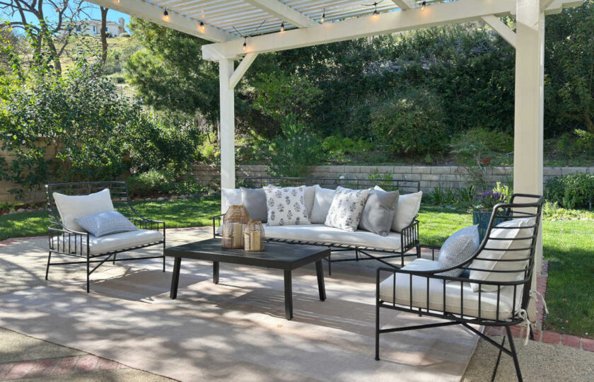 Covered outdoor patio space staged with a black metal sectional, patterned pillows, and string lights under a white pergola in Westlake Village.
