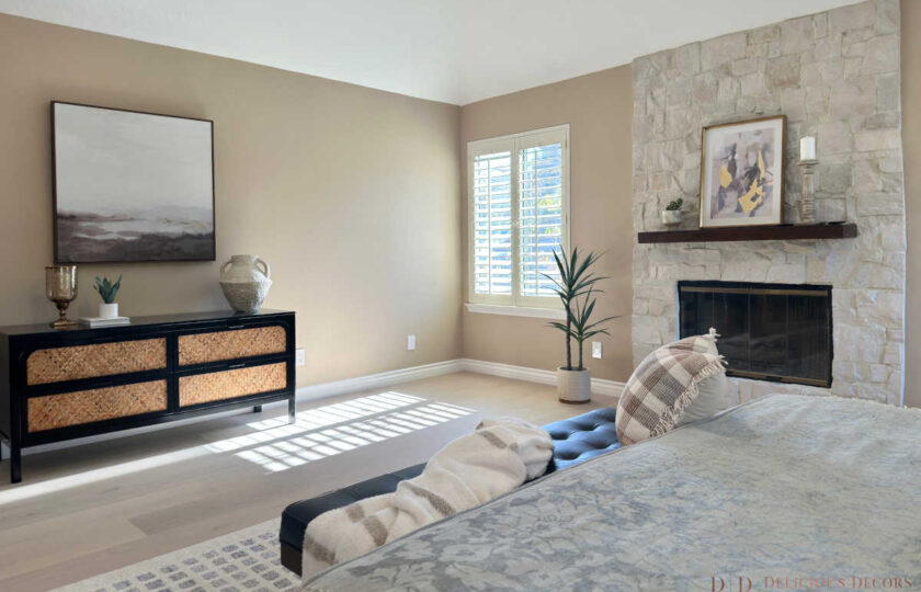 Primary bedroom suite view highlighting a stone fireplace, black cane-front dresser, landscape wall art, and light wood flooring in Westlake Village.