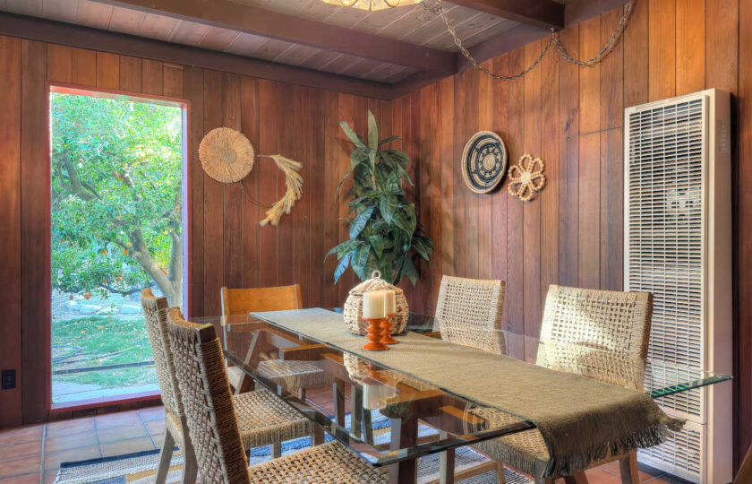 Mid-century modern dining room staging with glass table, woven chairs, wall sconces, and garden window view.