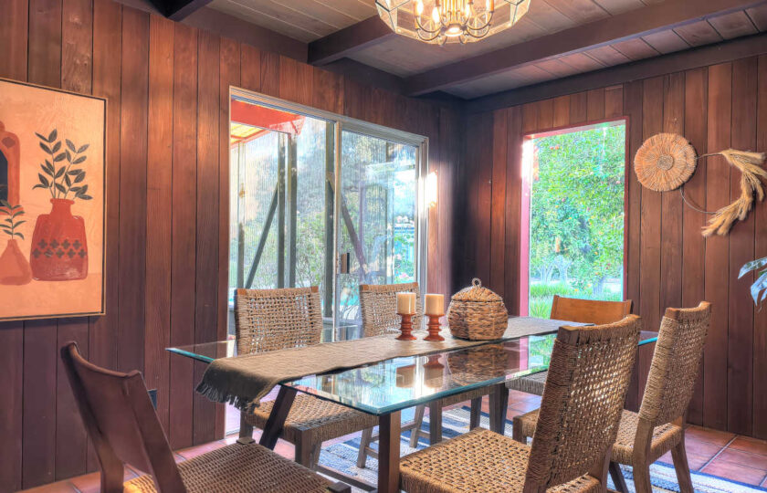Ojai MCM ranch dining space featuring glass dining table, original wood paneling, and natural light from glass slider.
