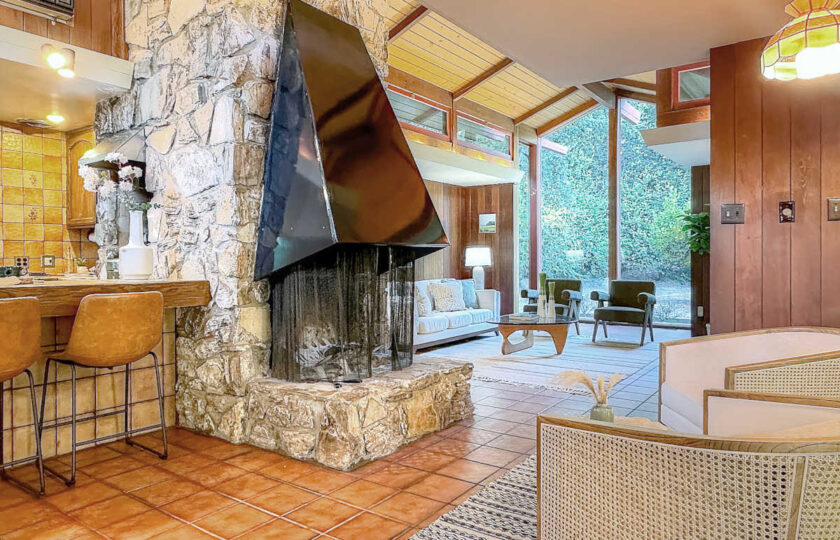 Staging Ojai MCM like it's 1957 featuring original freestanding stone fireplace, modern lounge chairs, and soaring beamed ceilings.