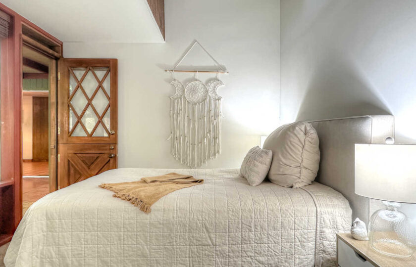 Guest bedroom staging in an Ojai MCM home with wall-mounted macrame art, neutral bedding, and vintage interior door.