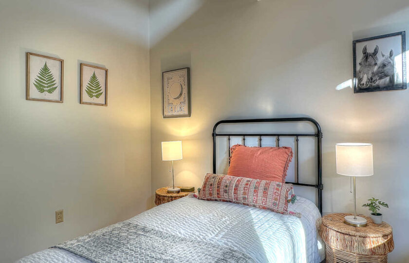 Cozy guest room staged with iron bed frame, boho throw pillows, and framed botanical prints in a 1957 Ojai house.