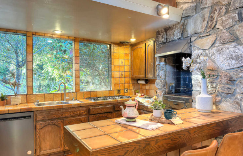 Staged 1957 mid-century modern kitchen with original stone masonry wall, tiled breakfast bar, and leather counter stools