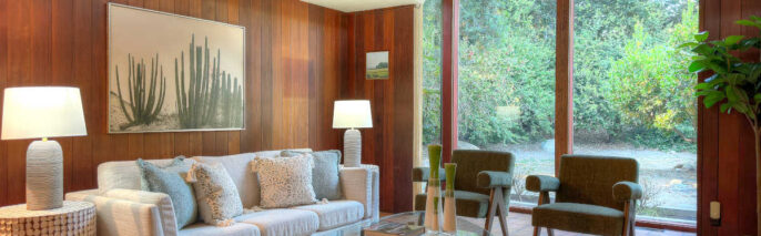 Ojai MCM living room staging showcasing full-length floor-to-ceiling windows, neutral sofa, and authentic wood paneled walls.