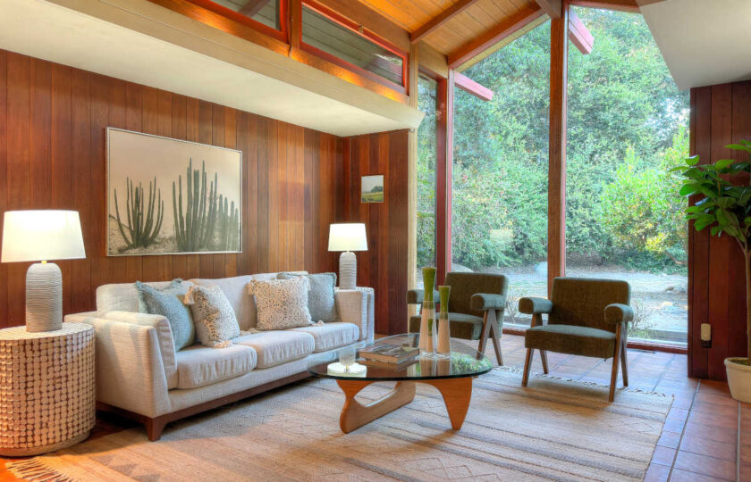 Ojai MCM living room staging showcasing full-length floor-to-ceiling windows, neutral sofa, and authentic wood paneled walls.