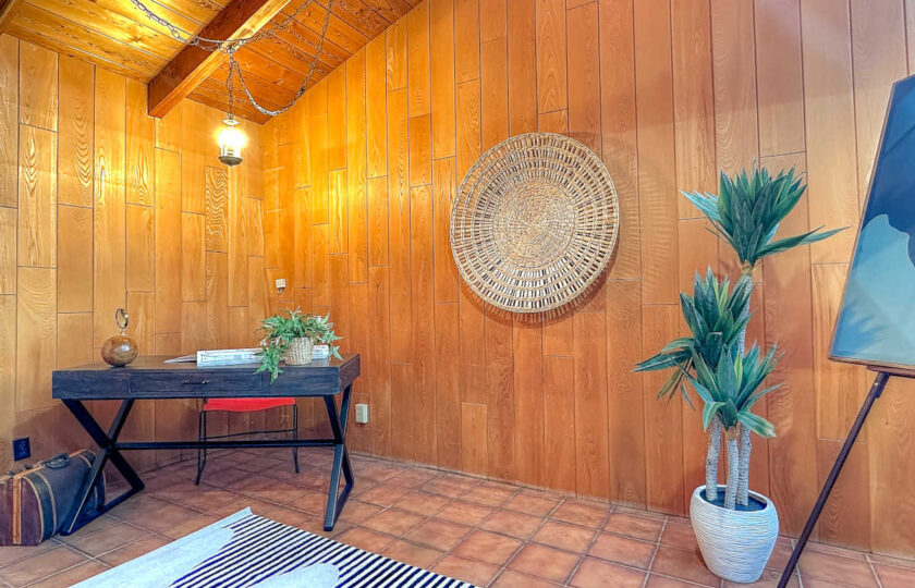 Staged mid-century modern home office with wooden desk, statement wall basket, and authentic wood paneling.