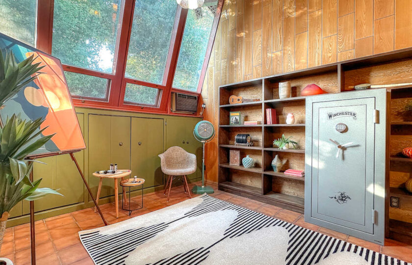 1957 MCM study featuring custom built-in shelving, angled window wall, geometric rug, and retro decor accents.