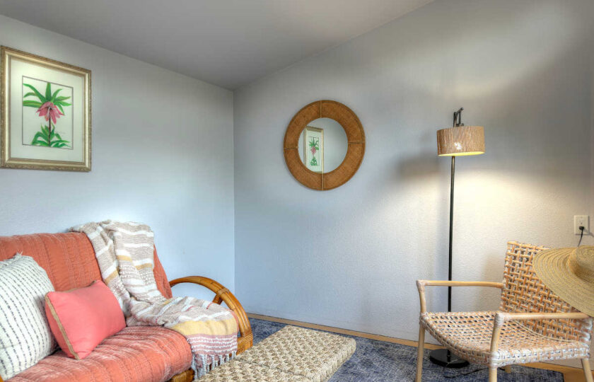 Staged pool house interior with coral futon sofa, rattan armchair, and neutral wall art.
