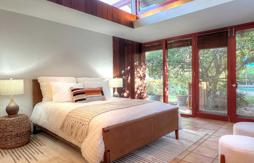 Ojai MCM primary bedroom staging with neutral bedding, clerestory windows, wooden headboard, and garden doors.