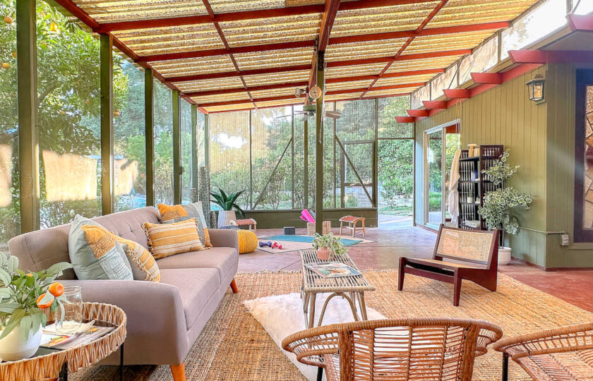 Expansive sunroom staging in a 1957 Ojai MCM home with corrugated roof structure, woven seating, and outdoor access.
