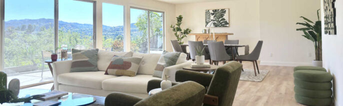 Woodland Hills MCM home staging featuring a sprawling great room, white sofa, olive armchairs, and hillside window views.