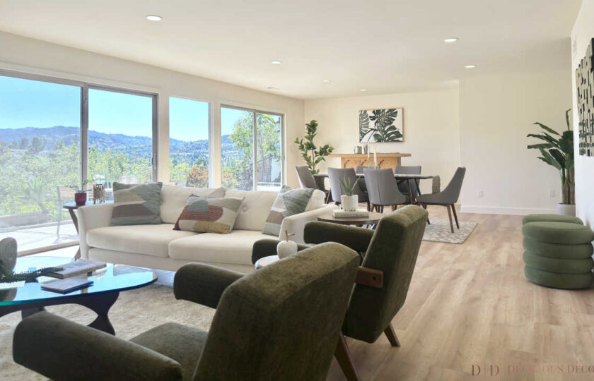 Woodland Hills MCM home staging featuring a sprawling great room, white sofa, olive armchairs, and hillside window views.
