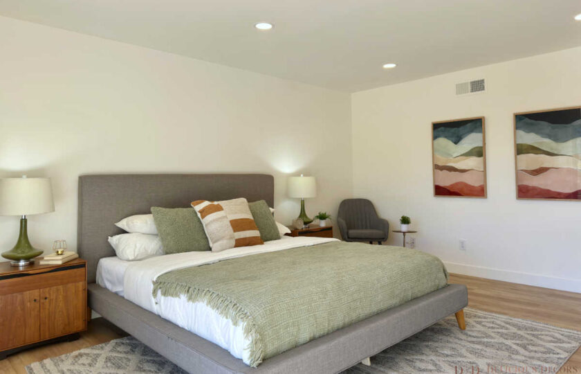 Woodland Hills MCM home staging featuring a grey bed, wood nightstands, lounge chair, and colorful abstract art.